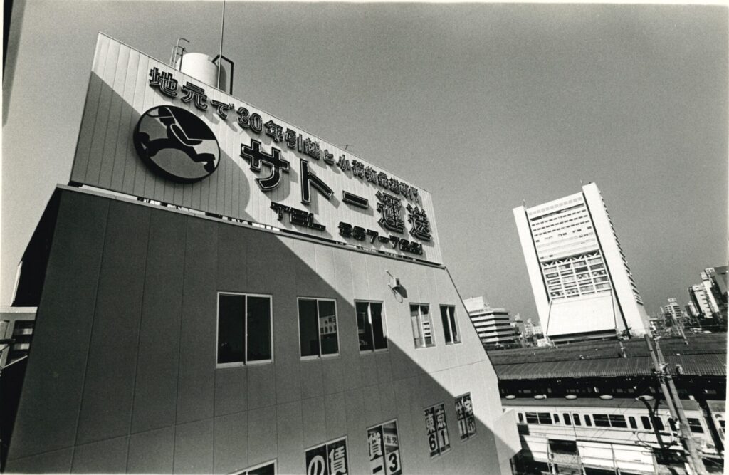 サトー運送創業30年時の社屋のモノクロ写真。向こう側に中野サンプラザが見える。