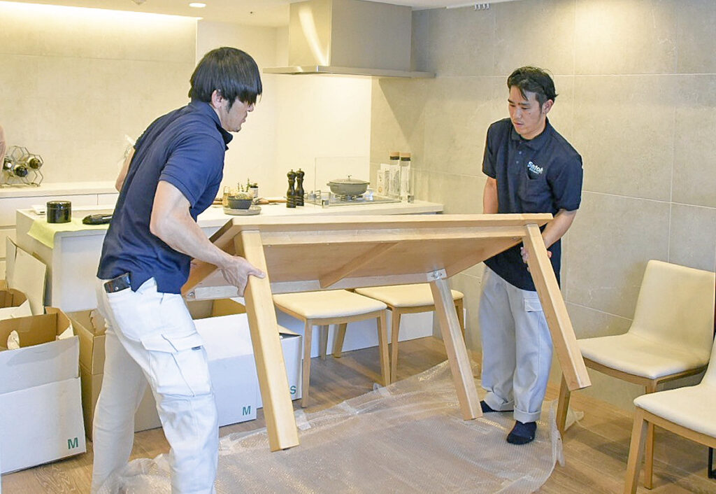 ダイニングテーブルを2人がかりで設置するサトー運送の作業員。