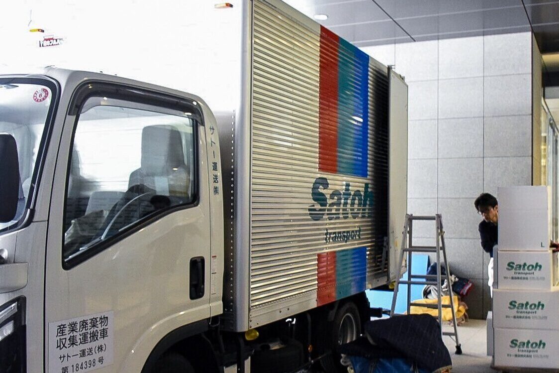 トラックから台車で荷物を運び出すサトー運送の作業員。