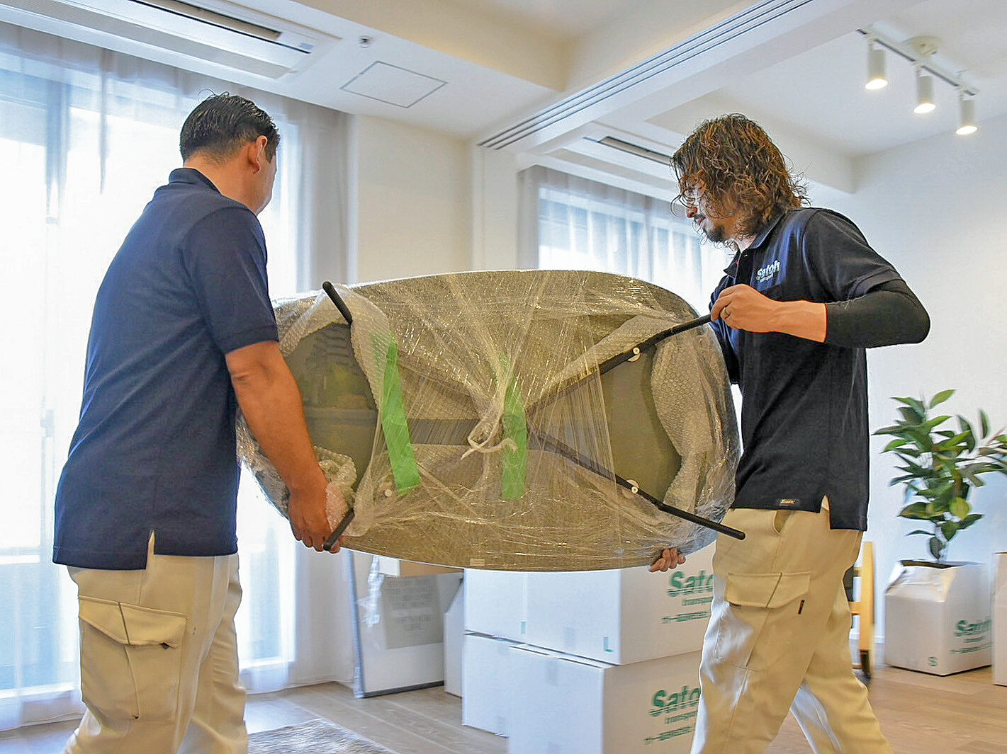 梱包されたセンターテーブルを部屋の中で運ぶサトー運送の作業員2人。